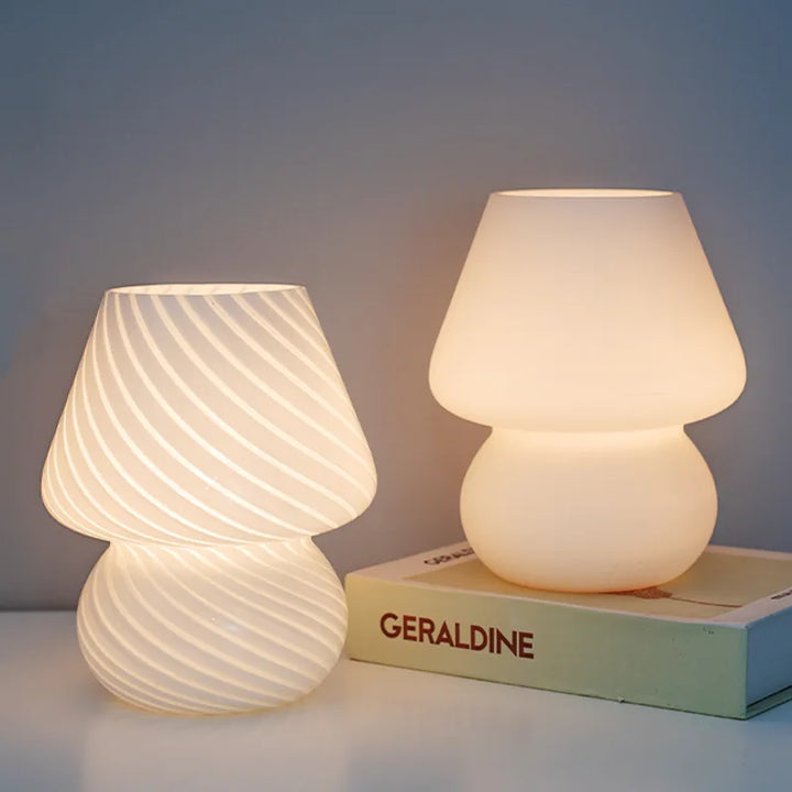 Two illuminated white table lamps with rounded, hourglass-shaped bases and shades.